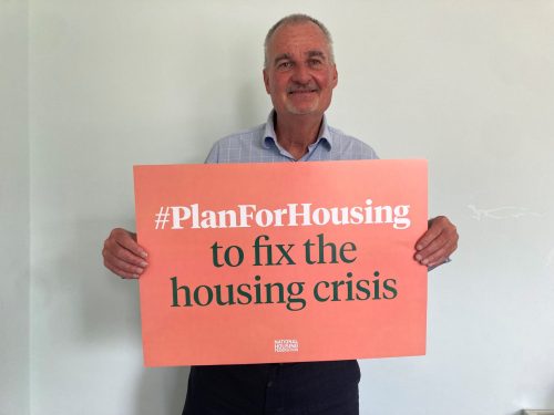BHT Sussex Chief Executive, David Chaffey, a white man in his early 60s, supports the #PlanForHousing campaign by holding a light red campaign placard that reads '#PlanForHousing to fix the housing crisis'.